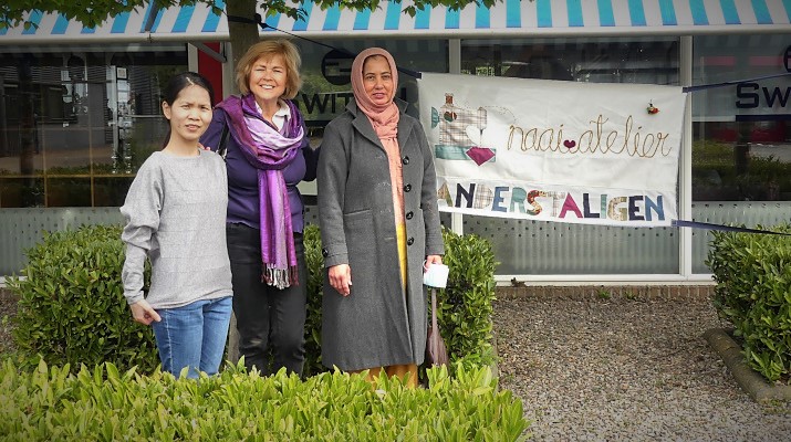 3 vrouwen naast spandoek met tekst Naaiatelier Anderstaligen